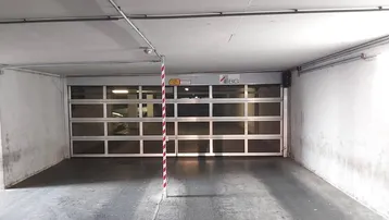 Saubere und gut beleuchtete Tiefgarageneinfahrt mit automatischem Rolltor und Betonboden.