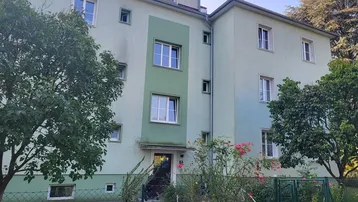 Mehrfamilienhaus mit hellgrüner Fassade und gepflegter Grünanlage im Vordergrund.