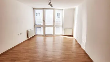 Helles, leeres Zimmer mit Laminatboden und großen Fenstern, bereit zur individuellen Gestaltung.