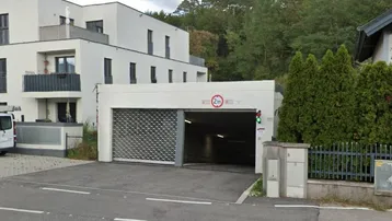 Tiefgarageneinfahrt mit Rolltor und Höhenbegrenzung, umgeben von moderner Wohnbebauung und Bäumen.