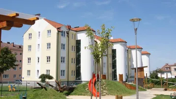Modernes Wohngebäude mit heller Fassade und einem Spielplatz im Vordergrund unter blauem Himmel.