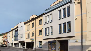 Reihe von Gebäuden entlang einer gepflasterten Straße mit Geschäften im Erdgeschoss und Wohnungen darüber.