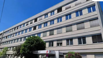 Modernes Bürogebäude mit mehreren Stockwerken und zahlreichen Fenstern unter blauem Himmel.