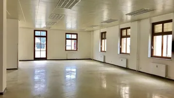 Geräumiger, leerer Büroraum mit vielen Fenstern und hellem Betonboden, ideal für gewerbliche Nutzung.