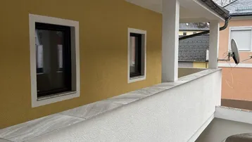Gebäudefassade mit gelbem Putz und einem überdachten Balkonbereich im Obergeschoss.