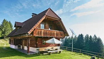 Traditionelles Holzhaus im alpinen Stil mit Balkon und Solaranlage auf einer grünen Wiese.