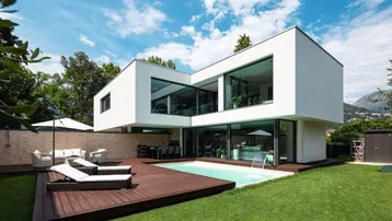 Moderne Villa mit großzügigem Garten, privatem Pool und Holzterrasse unter blauem Himmel.