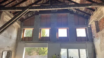 Großer Innenraum im Rohbau mit sichtbarer Holzdachkonstruktion und vielen Fenstern.