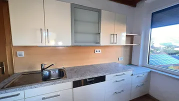 Funktionale Küche mit hellen Schränken, Spülmaschine und Fenster mit Weitblick.