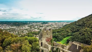 Luftaufnahme einer historischen Burgruine mit weitem Blick über eine Stadt und bewaldete Hügel.