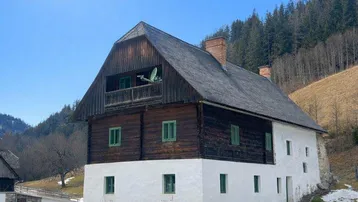 Traditionelles Bauernhaus mit Holzbalken und weiß getünchter Fassade in alpiner Landschaft.