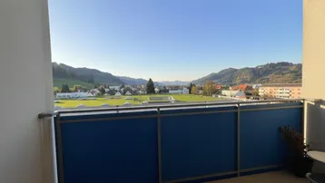 Geräumiger Balkon mit blauer Brüstung und weitem Blick auf die umliegende Landschaft und Berge.