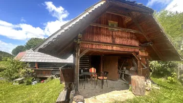 Eine rustikale Holzhütte mit überdachtem Eingangsbereich und kleiner Sitzgelegenheit im Freien.