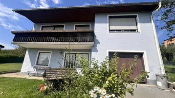 Zweistöckiges Haus mit hellblauer Fassade, Balkon und integrierter Garage unter blauem Himmel.