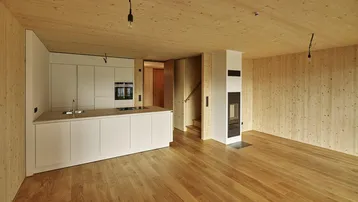 Moderner offener Wohnbereich mit integrierter Küche, Holzboden und Kaminofen.