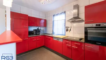 Moderne Küche mit roten Hochglanzfronten, integrierten Geräten und Fliesenboden.