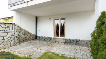 Gepflasterte Terrasse mit Steinmauer und Zugang zum Gartenbereich.