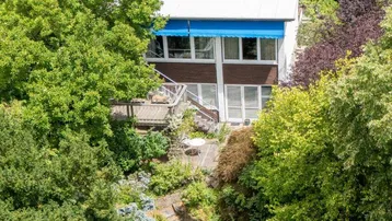 Luftaufnahme eines Hauses mit weitläufigem Garten und blauer Markise, umgeben von üppigem Grün.