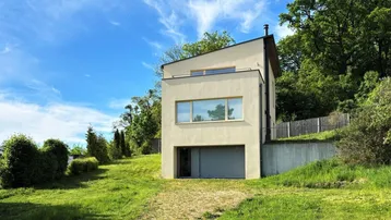 Modernes Einfamilienhaus mit heller Fassade, Garage und großem Grundstück in grüner Umgebung.