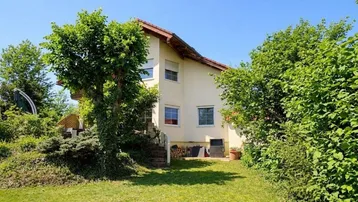Einfamilienhaus mit großem Garten und viel Grünfläche unter blauem Himmel.