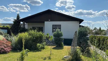 Einfamilienhaus mit gepflegtem Vorgarten und weißer Fassade unter blauem Himmel.