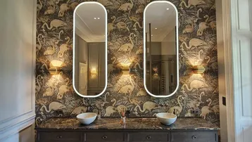 Elegantes Badezimmer mit doppelten Waschbecken, gemusterter Tapete und stilvollen Wandleuchten.