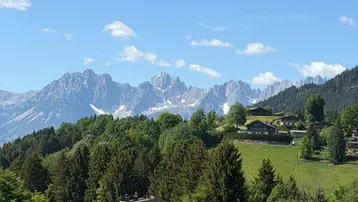 Panoramablick auf die majestätischen Berge und grüne Hügel mit traditionellen Häusern unter blauem Himmel.
