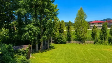 Weitläufiger grüner Garten mit hohen Bäumen und Blick auf die umliegende Landschaft.