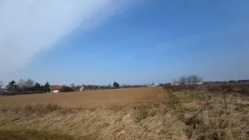 Weite Felder und trockene Gräser unter einem klaren blauen Himmel mit vereinzelten Häusern in der Ferne.