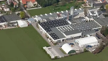 Luftaufnahme eines weitläufigen Industriekomplexes mit mehreren Gebäuden und angrenzenden Grünflächen.