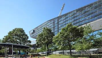 Moderne Architektur des Bürogebäudes mit großen Glasflächen und umliegender Grünanlage unter blauem Himmel.