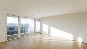 Helles Wohnzimmer mit Parkettboden, großen Fenstern und Zugang zu einem Balkon.