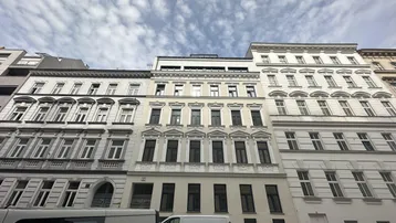 Historische Fassade eines Mehrfamilienhauses in der Stadt mit modernen Dachaufbauten.