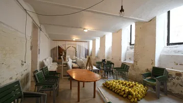 Geräumiger Kellerraum mit weiß gestrichenen Ziegelwänden, kleinen Fenstern und einfacher Beleuchtung, eingerichtet für eine Veranstaltung.