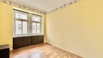 Heller Raum mit gelben Wänden, Laminatboden und zwei Fenstern mit Blick nach draußen.