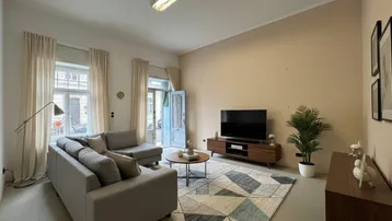 Gemütliches Wohnzimmer mit Sofa, Fernseher und Zugang zu einem französischen Balkon.