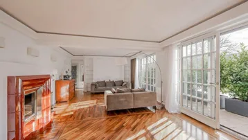 Helles Wohnzimmer mit elegantem Parkettboden, Kamin und Zugang zu einer Terrasse.
