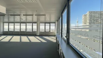 Geräumiges, leeres Büro mit großen Fenstern, die viel Tageslicht hereinlassen und einen weiten Stadtblick bieten.