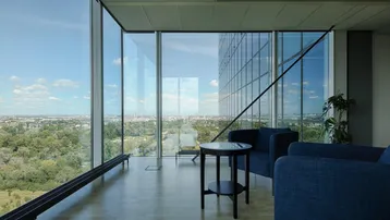 Moderner Loungebereich mit raumhohen Fenstern, die einen weiten Blick auf die Stadt und die grüne Umgebung bieten.