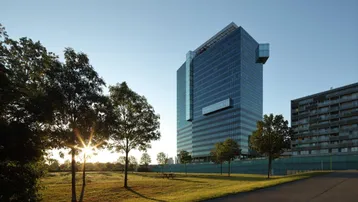 Modernes Bürogebäude mit Glasfassade und umliegender Grünfläche bei Sonnenuntergang.