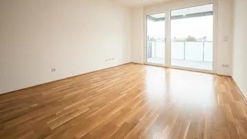 Helles Zimmer mit Parkettboden und Zugang zu einem Balkon, ideal als Wohn- oder Schlafbereich.