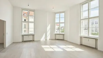Heller, leerer Raum mit großen Fenstern, die viel Tageslicht hereinlassen und einem hellen Holzboden.