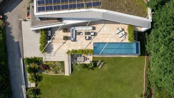 Luftaufnahme der modernen Villa mit Pool, großer Terrasse, Solaranlage und Gründach.