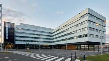 Modernes Bürogebäude mit klarer Architektur, großen Fensterfronten und weitläufigen Parkflächen.