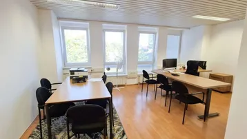 Helles Büro mit mehreren Arbeitsplätzen, Holzboden und großen Fenstern mit Blick ins Grüne.