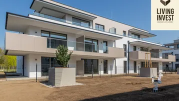 Modernes Mehrfamilienhaus mit weißer Fassade, Balkonen und noch ungestaltetem Gartenbereich.