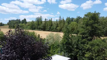 Weitläufiger Blick über Felder und Wälder unter einem strahlend blauen Himmel mit weißen Wolken.