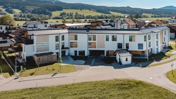 Moderne Neubau-Wohnanlage mit weißer Fassade und Holzakzenten in einer grünen, ländlichen Umgebung.