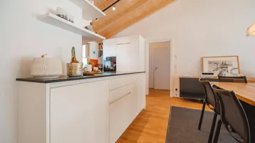 Moderne weiße Küche mit dunkler Arbeitsplatte, integrierten Geräten und Holzdecke im offenen Wohnbereich.