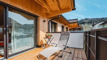 Sonniger Balkon mit Holzfußboden, Liegestuhl und weitem Blick auf die umliegende Landschaft.